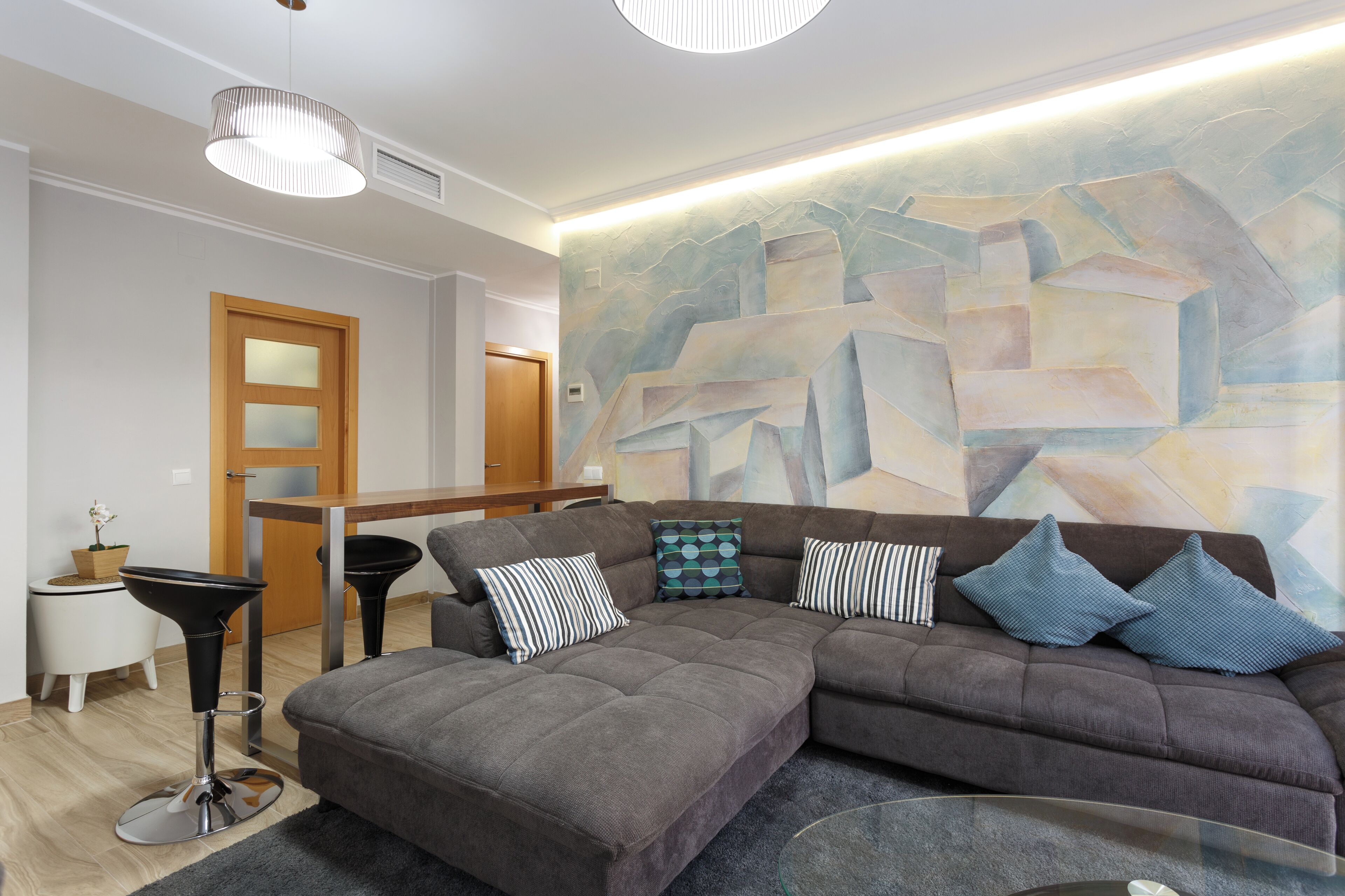 Een moderne woonkamer met een modulaire bank, een glazen salontafel, een barstoel en een moderne abstracte muurschildering.