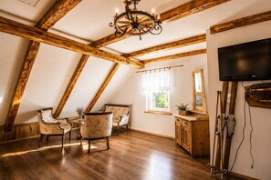 A room with wooden beams, a chandelier, a TV, and two chairs.