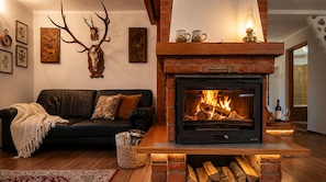 A cozy living room with a fireplace, a black leather sofa, and a rustic decor including antler wall art.