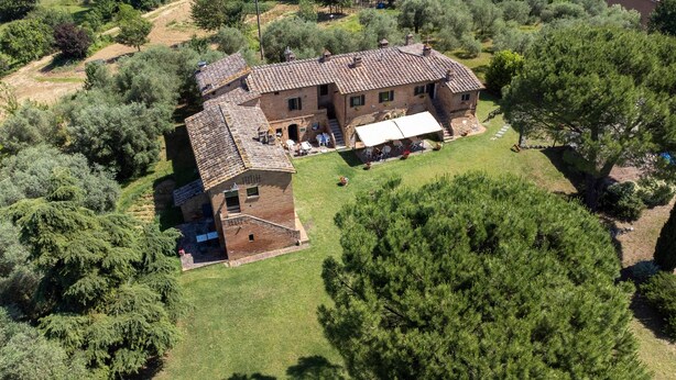 Vue aérienne d’une maison de campagne en pierre, avec un toit en tuiles, entourée d’une végétation luxuriante et d’arbres.