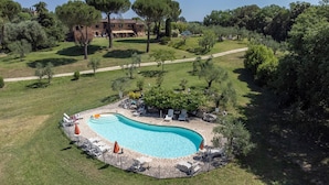 Une piscine entourée d’une terrasse en pierre, avec des chaises longues et des parasols.