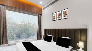 Een hotelkamer met een groot raam, een bed met zwart-wit beddengoed, een nachtkastje met een lamp en drie ingelijste foto's aan de muur.