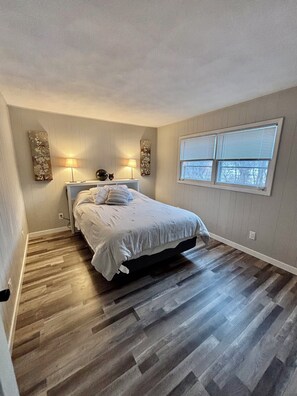 A bedroom with a bed, two wall-mounted lamps, a window with blinds, and a wooden floor. - 3-bedroom scenic condo (Janesville)