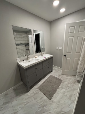 A bathroom with a double sink vanity, a large mirror, a towel rack, and a door.