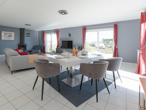 A modern living room with a sofa, a dining table with chairs, a TV, and a fireplace. - House in Saint-pabu Near Stunning Beaches (Saint-Pabu)