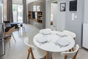 Ein stilvoller Essbereich mit einem runden Tisch für vier Personen, einer Couch und einem Fernseher im Hintergrund.