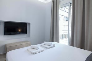 Ein Hotelzimmer mit Bett, einem Flachbildfernseher an der Wand, einer Sitzbank und einem Fenster mit Vorhängen.