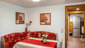 A dining area with a red and white table, two framed floral paintings, and a wooden door leading to a kitchen.