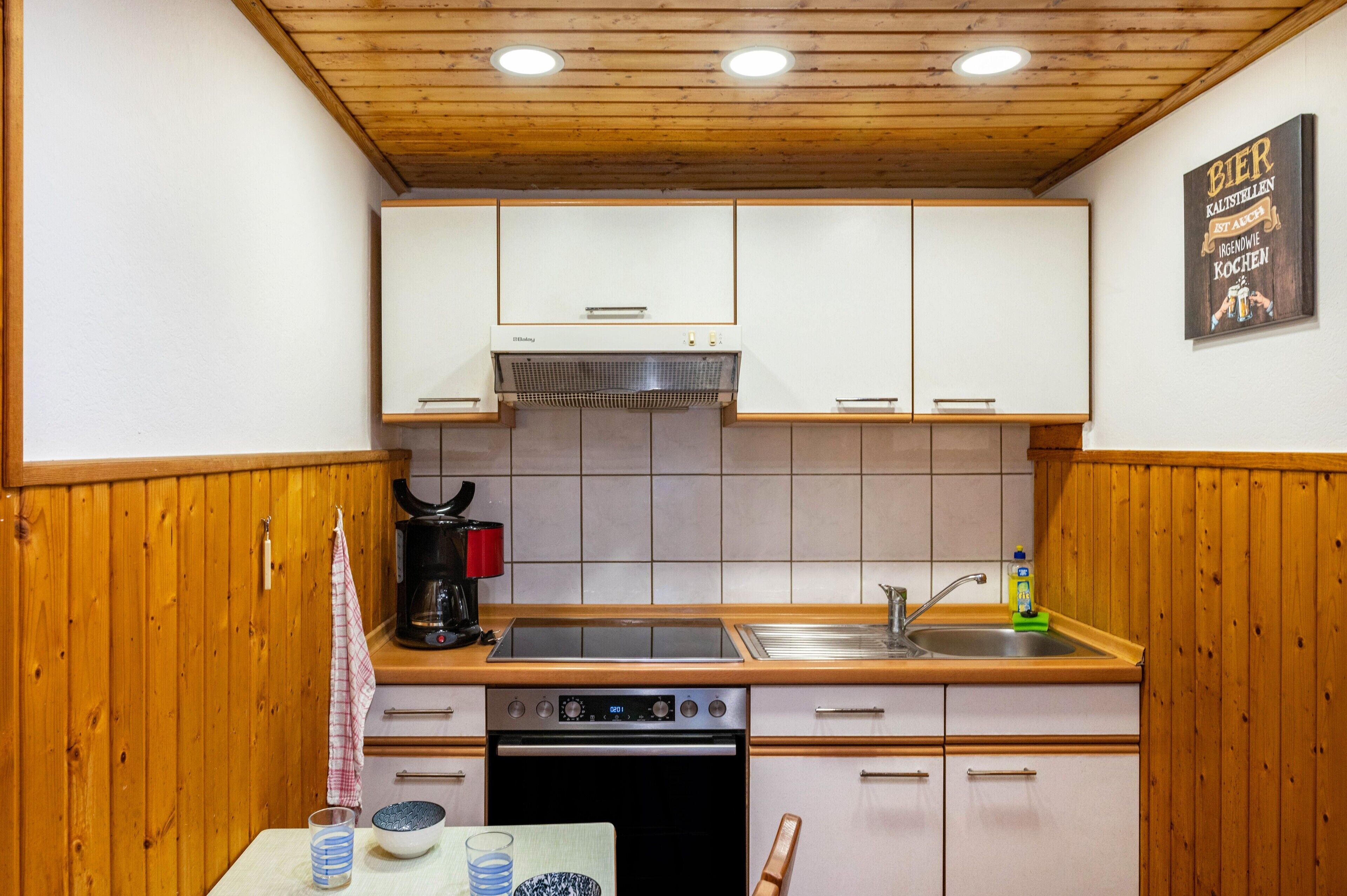 Una cocina compacta con armarios de madera, horno integrado, cafetera y lavamanos.
