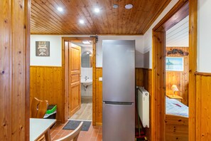Een houten interieur met een eethoek, een koelkast, en een badkamer die door een open deur zichtbaar is.