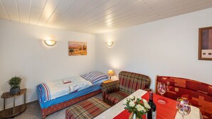 Ein gemütliches Zimmer mit einem Bett, einem Sofa, einem kleinen Tisch mit Blumenvase und einem Gemälde an der Wand.