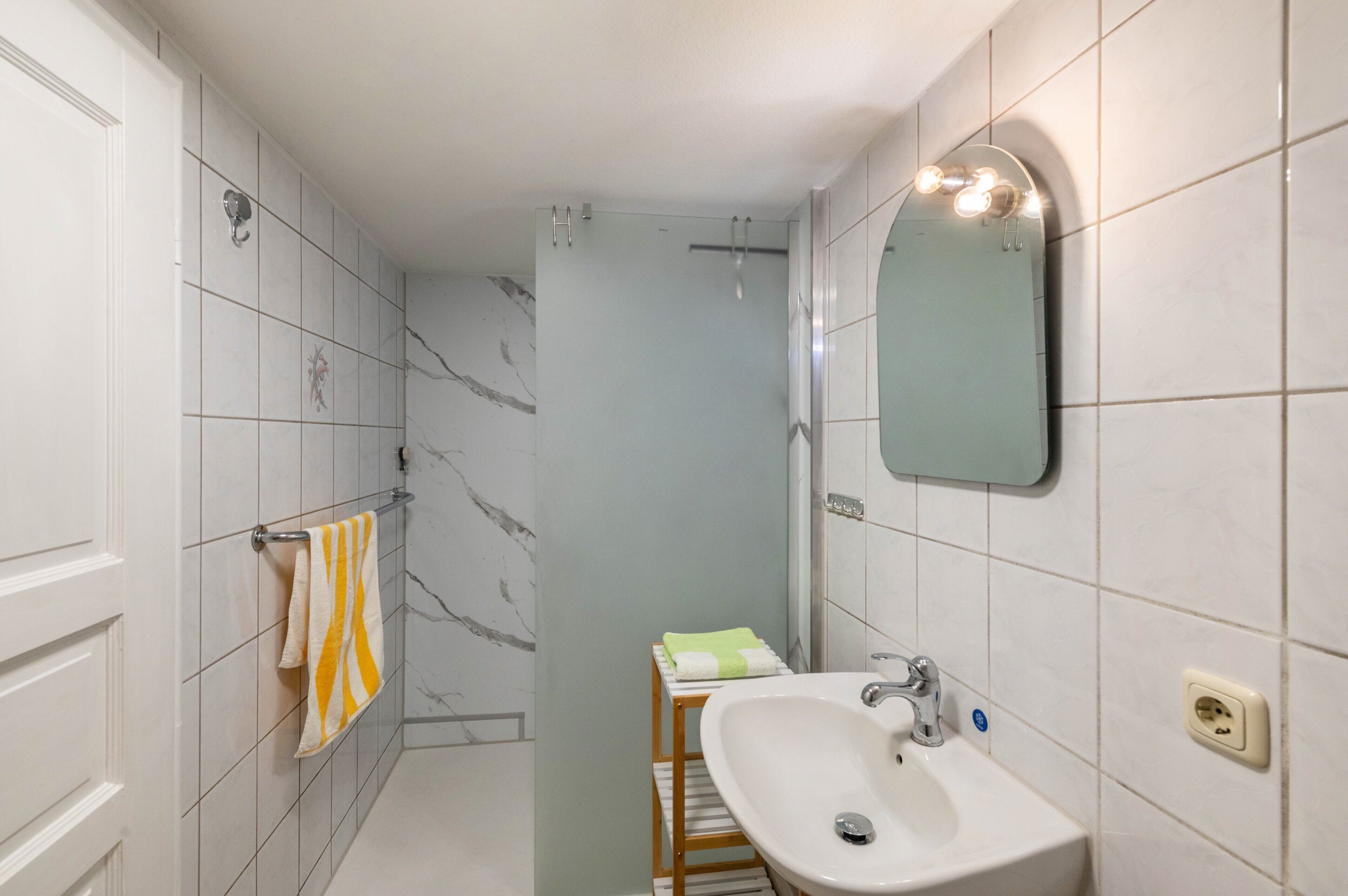 Ein Badezimmer mit weißem Waschbecken, einem Spiegel und einem Handtuchhalter.