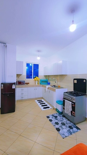 A compact kitchen with white cabinets, a refrigerator, a stove, and a window with a view. - Modern Coastal Apartment - Lift/Elevator Access,7 mins from beach, 24hr security (Mombasa)