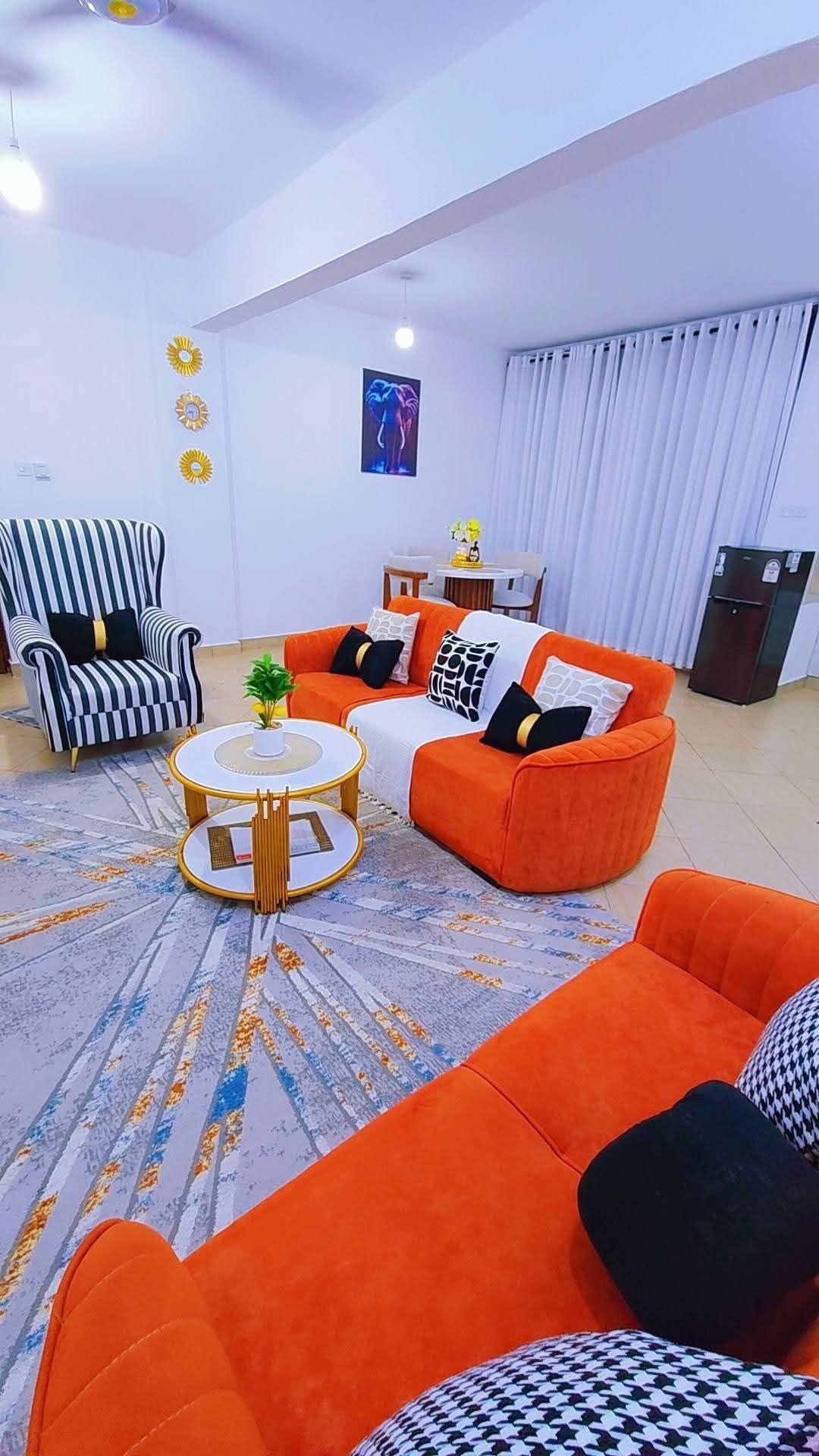 Ein Wohnzimmer mit einem gestreiften Sessel, einem orangefarbenen Sofa, einem runden Couchtisch und einem Bild an der Wand.
