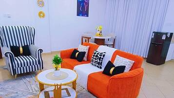 Ein Wohnzimmer mit einem gestreiften Sessel, einem orangefarbenen Sofa, einem runden Couchtisch und einem Bild an der Wand.