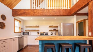 Uma cozinha moderna com uma ilha de madeira, banquetas e vista para o andar superior.