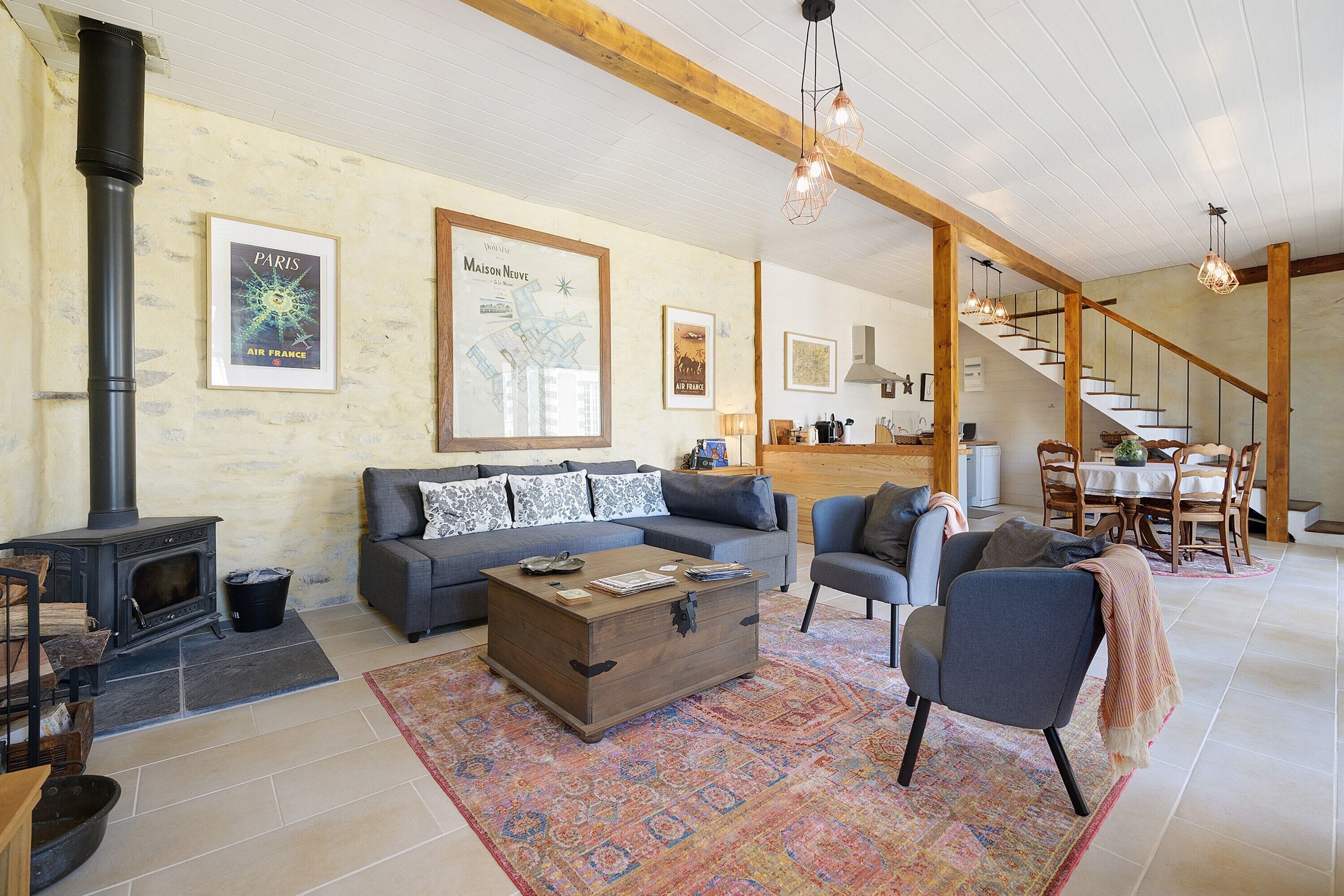 A living room with a fireplace, sofa, armchair, and a dining area with a staircase.