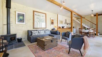 A living room with a fireplace, sofa, armchair, and a dining area with a staircase.