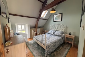 Quarto com teto inclinado, cama com roupa de cama estampada, mesa de cabeceira com abajur e janela com vista.