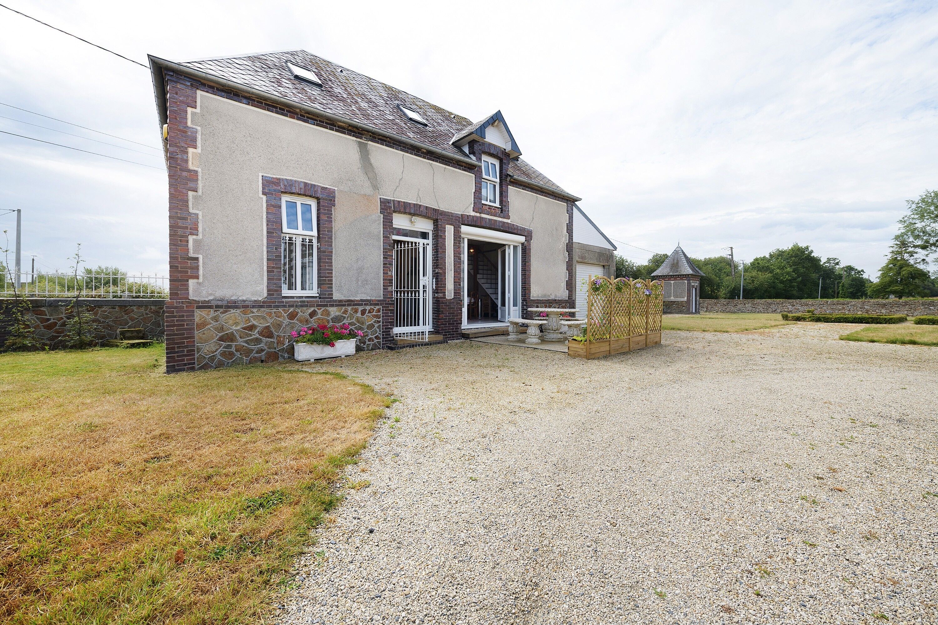 A two-story house with a gravel driveway, a stone wall, and a small garden area.