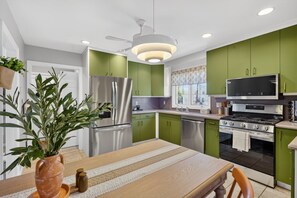 Una cocina moderna con armarios verdes, electrodomésticos de acero inoxidable y un ventilador de techo.