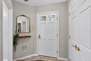 A hallway with a white door, a mirror, a plant, and a shelf.