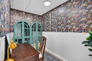 Una habitación con una mesa de madera, un aparador verde azulado y un papel tapiz floral.