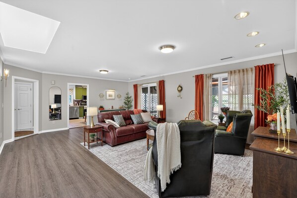 Un salón espacioso con piso de madera oscura, un sofá de cuero rojo, un sillón negro y una zona de comedor con una mesa y sillas de madera.