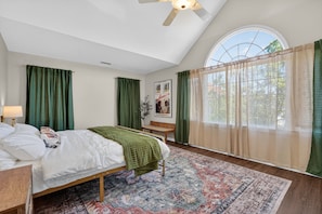 Un dormitorio con cama, un banco, una ventana con cortinas y un ventilador de techo.