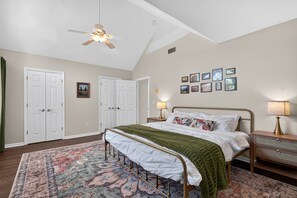 A bedroom with a bed, a ceiling fan, a nightstand with a lamp, a dresser, and a wall with framed pictures.
