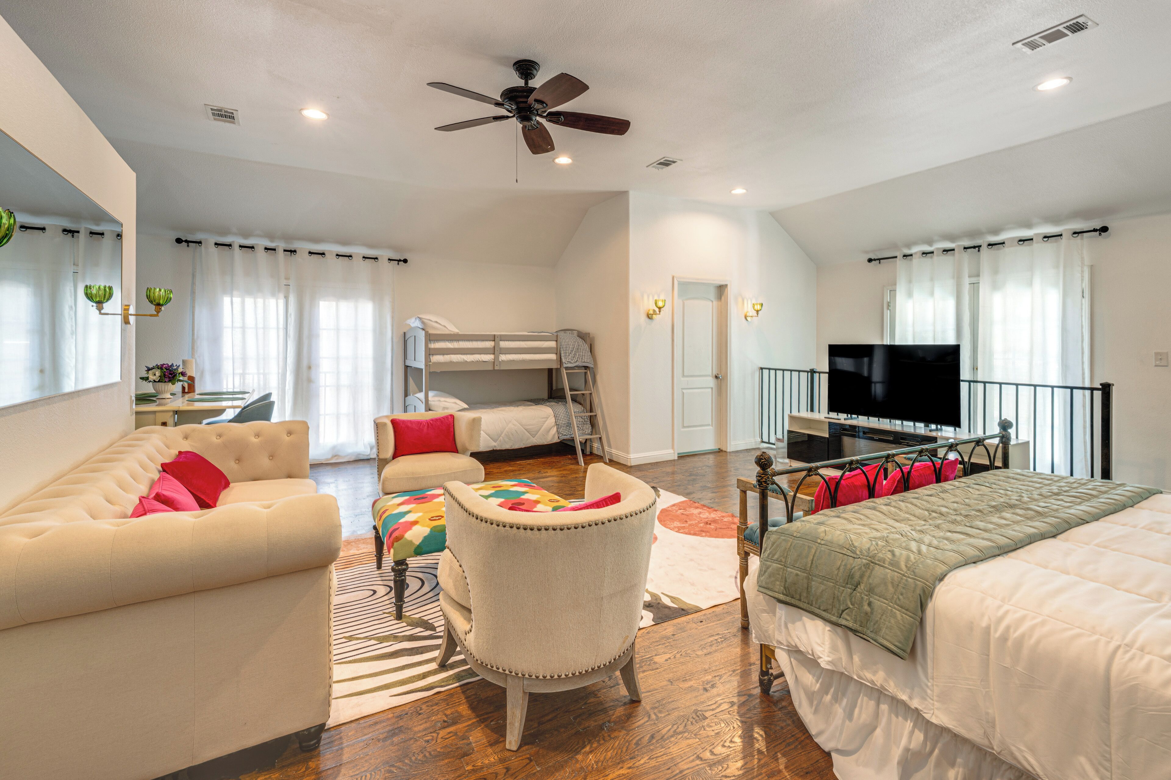 A bedroom with a bunk bed, a sofa, a chair, a television, and a ceiling fan.