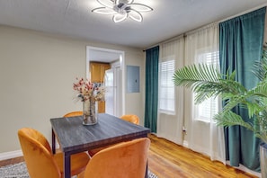 A dining area with a wooden table and orange chairs, a vase with dried flowers, and a large plant.