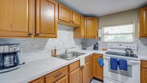 A kitchen with wooden cabinets, a stainless steel sink, a stove, and a coffee maker.