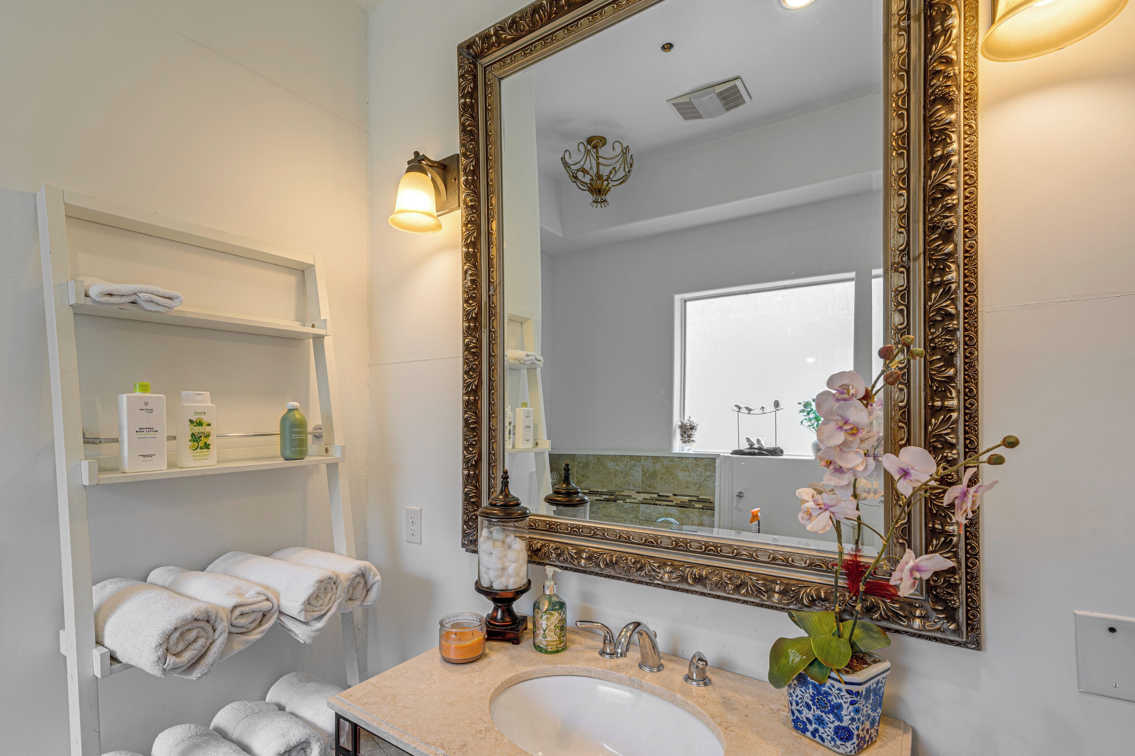 Une salle de bain dotée d’un grand miroir décoratif, d’un lavabo et d’étagères où sont rangées des serviettes et des articles de toilette.