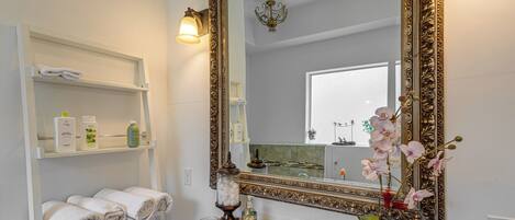 A bathroom with a large ornate mirror, a sink, and shelves with towels and toiletries.