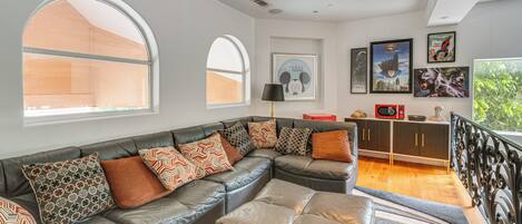 A modern living room with a sectional sofa, large windows, and a staircase leading to an upper level.