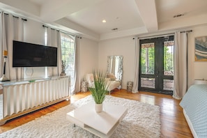 A spacious room with a large flat-screen TV, a white console table with a plant, a sofa, and a bed.