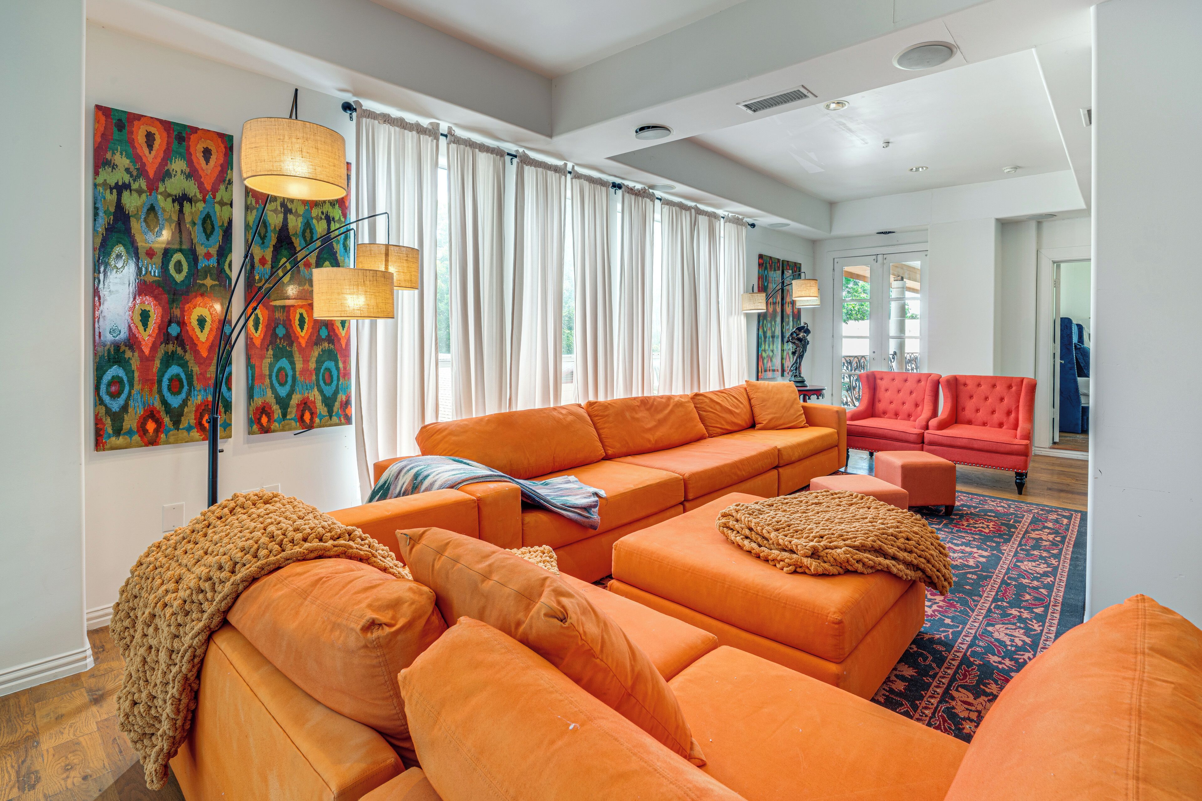 A living room with orange sofas, a red chair, and a large window with curtains.