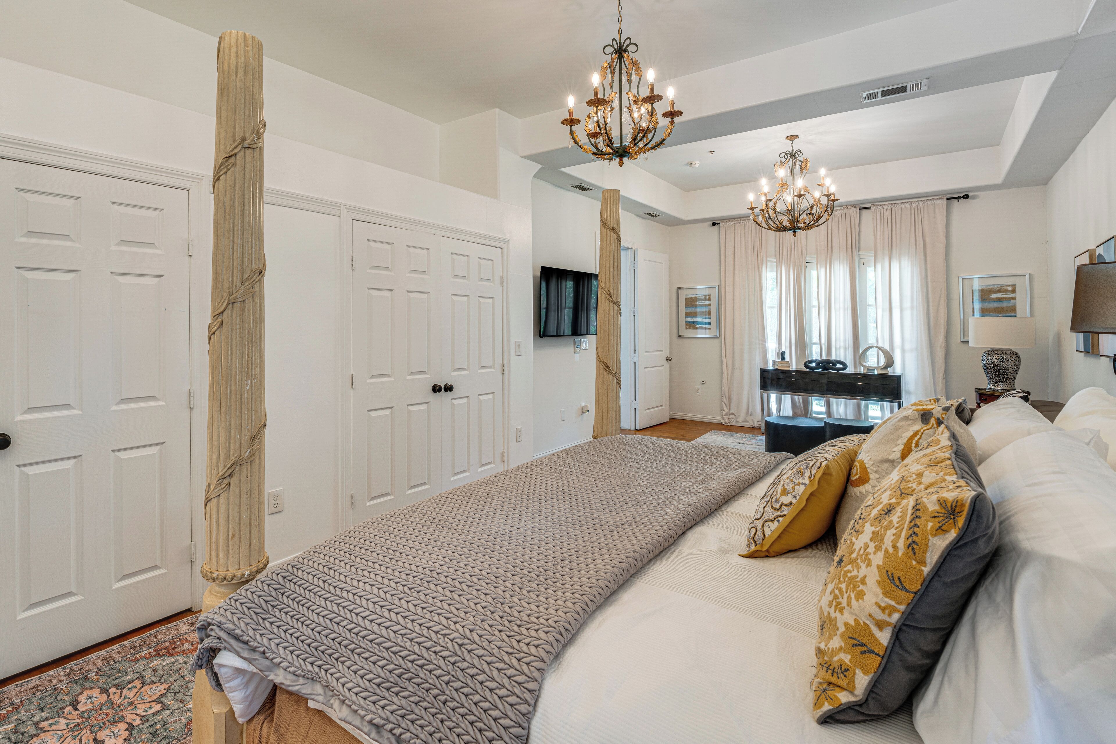 A bedroom with a large bed, a chandelier, a TV, and a desk with a chair.