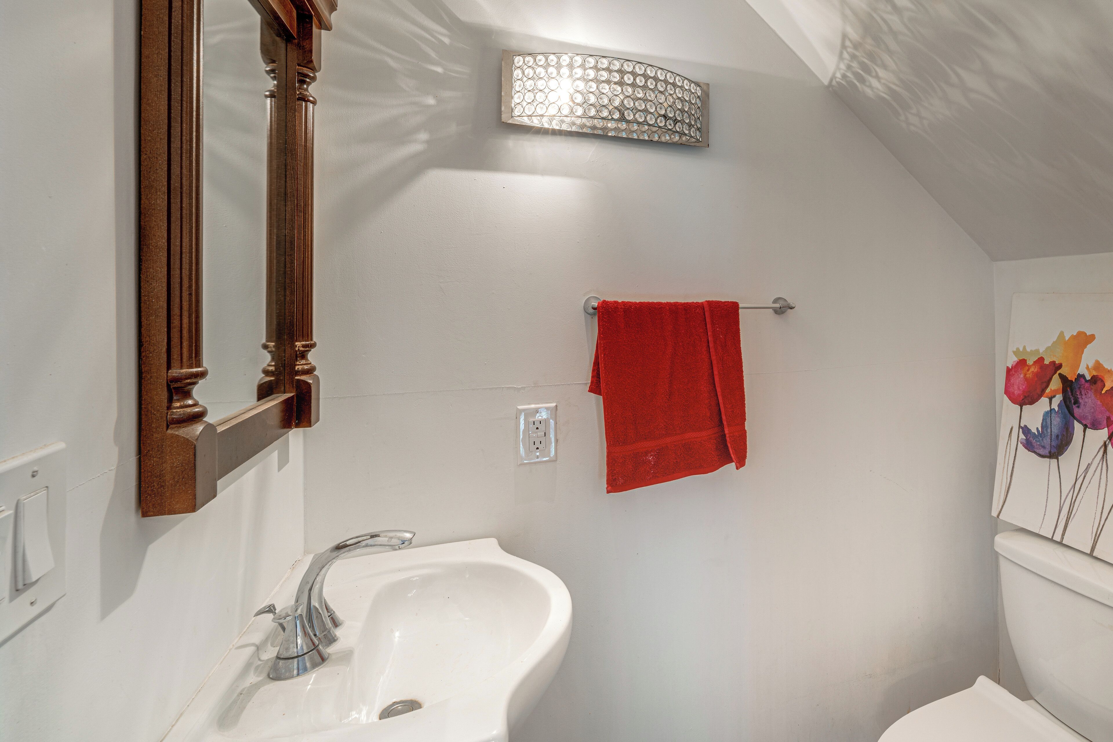 A bathroom with a white sink, a mirror, a red towel, and a wall-mounted light fixture.