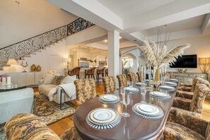 A spacious living area with a dining table set for six, surrounded by patterned chairs, a staircase, and a kitchen in the background. - Luxe Old East Dallas Home in Historic Munger Place (Dallas)