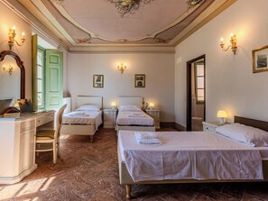 Une chambre d’hôtel avec deux lits simples, un bureau avec une chaise, une commode et un grand lit.
