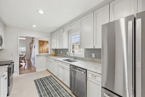 A modern kitchen with white cabinets, stainless steel appliances, a large refrigerator, and a window above the sink. - Springtide - 3-bedrooms - Newly Remodeled (Pawleys Island)