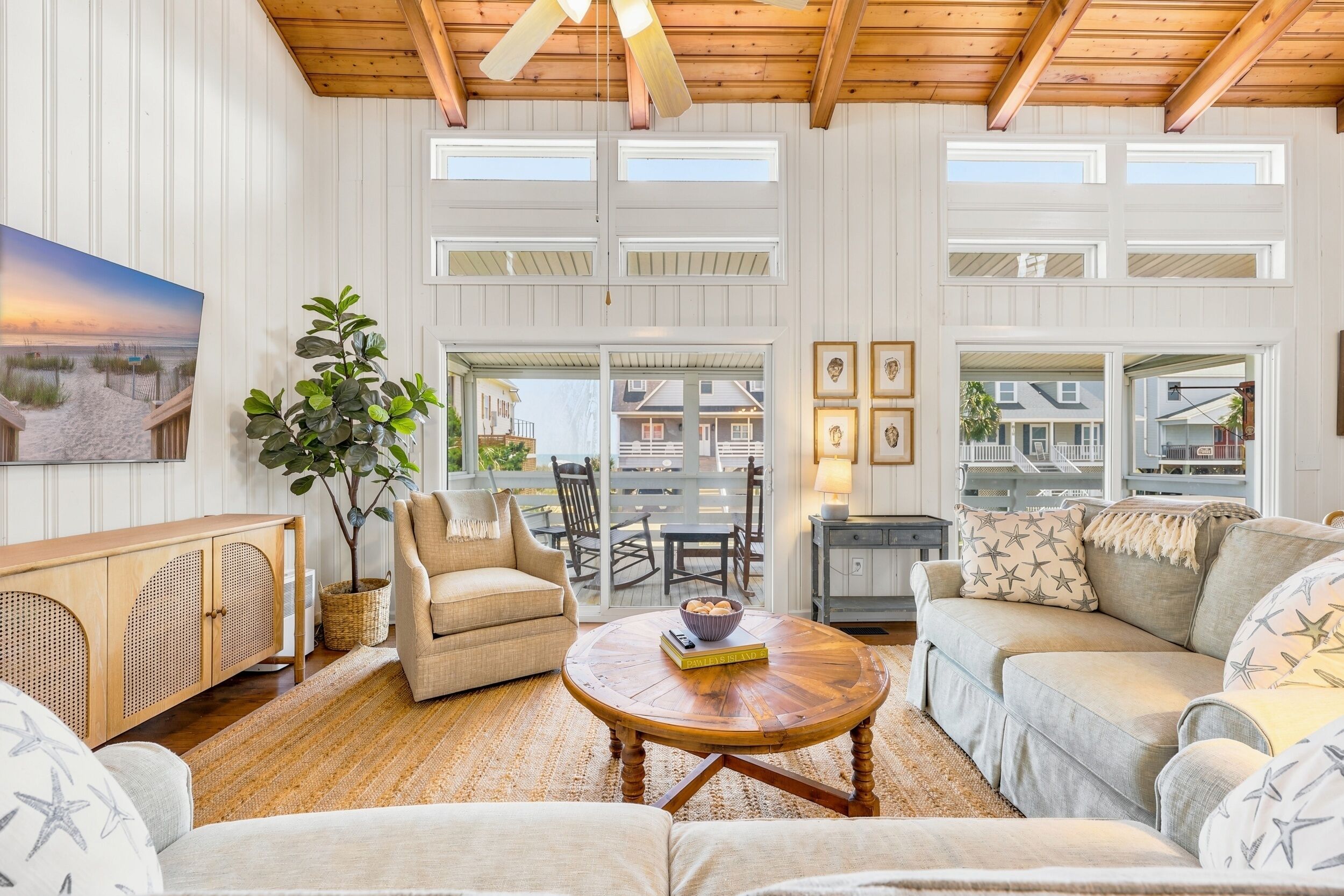 Un salon spacieux avec un plafond haut, de grandes fenêtres, un ventilateur de plafond en bois et un coin salon confortable avec une table basse.