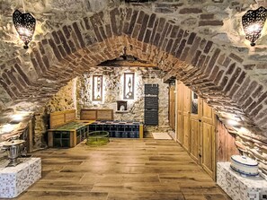 Ein Zimmer mit Steinwänden, einer hölzernen Bank, einem gefliesten Boden und einem Regal mit Flaschen.