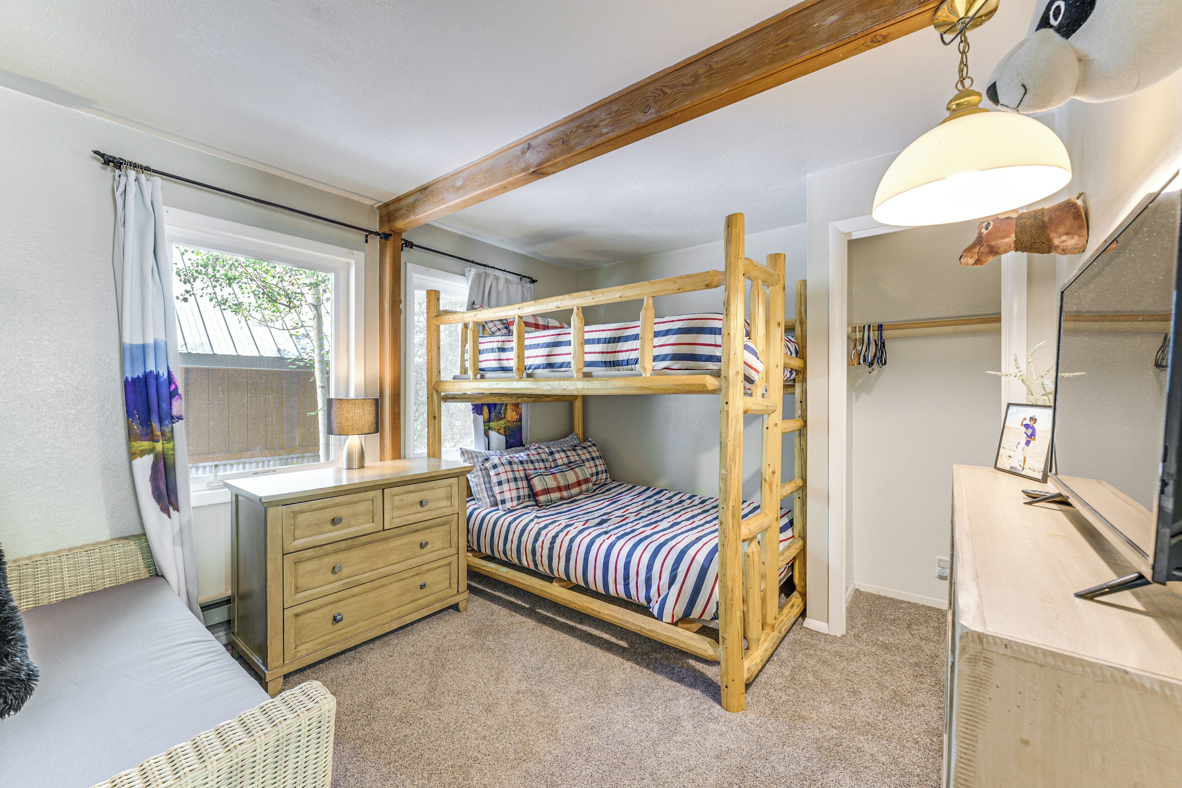 Een stapelbed met een gestreept dekbed, een houten dressoir, een spiegel en een hanglamp.