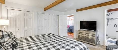 Une chambre à coucher avec une couvre-lit à carreaux, un téléviseur, une commode et une porte donnant sur une salle de bain.