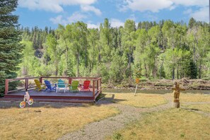 Une terrasse agrémentée de chaises Adirondack aux couleurs vives, d’une clôture en bois et d’un panneau indicateur, le tout situé dans une zone boisée.