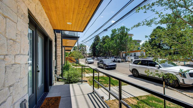 A building with a stone facade, a wooden ceiling, and a metal railing overlooking a street with parked cars.