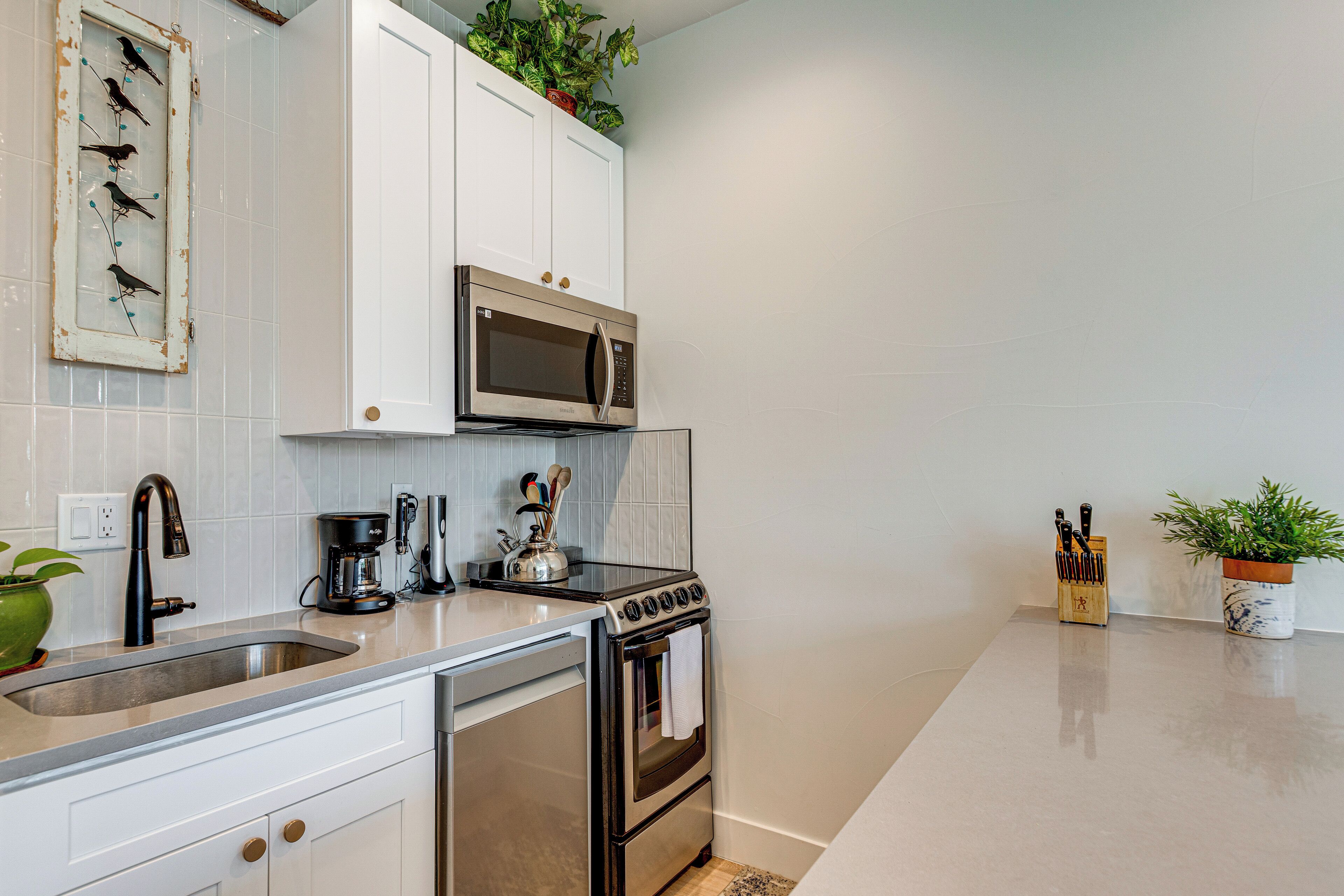 A modern kitchen with white cabinets, stainless steel appliances, a coffee maker, and a knife block.
